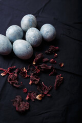 Beautiful DIY blue painted Easter eggs, dry Hibiscus tea flowers. Easter black fabric background. Vertical close up shot