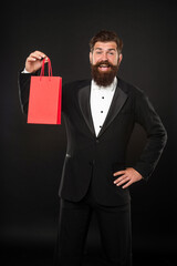 surprised man in tuxedo bow tie on black background with purchase shopping bag. copy space.