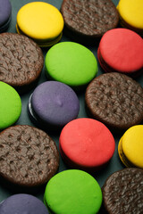 Chocolate cookies and macaroons of different colors lie on a dark background
