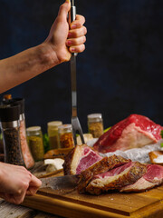 A professional chef prepares tenderloin meat steaks on a dark background. Lots of ingredients on the kitchen table. Recipes for home and restaurant cuisine. Organic food, holiday dish.