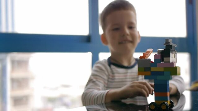 View of a assembled construction set colorful plastic toy constructor blocks game. A happy kid near the window on the background.
