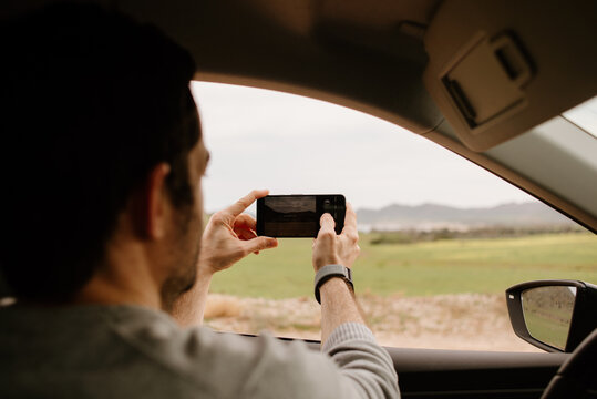 On a road trip. Young man stops the car to take a photo of the landscape sunset.