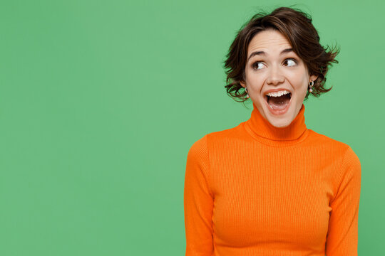 Young amazed surprised fun woman 20s wear casual orange turtleneck look aside on workspace area mock up isolated on plain pastel light green color background studio portrait. People lifestyle concept.