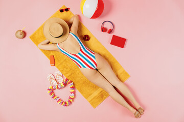 Top back view full body young woman wearing striped one-piece swimsuit cover face with hat lies on towel hotel pool isolated on plain pink color background. Summer vacation sea rest sun tan concept. © ViDi Studio