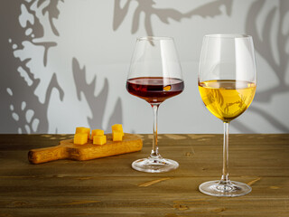 Glass of white wine, glass of red wine and cheese plate on wooden background, copy space