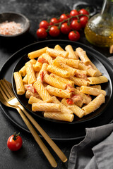 Tortiglioni with tomatoes, ricotta and basil in a black plate on a dark kitchen table. Traditional Italian pasta with vegetables and creamy cottage cheese on a culinary background