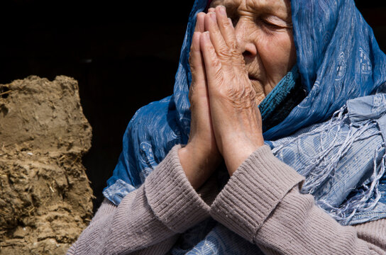 An old woman prays for peace in Ukraine. Grandmother prays for an end to the war. War in Ukraine. A woman prays in front of a destroyed house. Consequences of the war in Ukraine. Ukrainian refugees