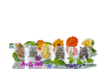 Glass jars of food supplements surrounded by medicinal plants on white.