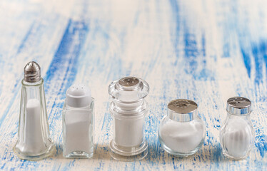 Fine salt under various transparent glass salt shakers aligned.