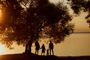 A silhouette of a happy family standing against the sunset near a tree