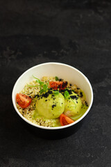 Bowl with bulgur, tomatoes, chicken meatballs and broccoli sauce in eco paper container on black background. Healthy food delivery service and daily ration concept.