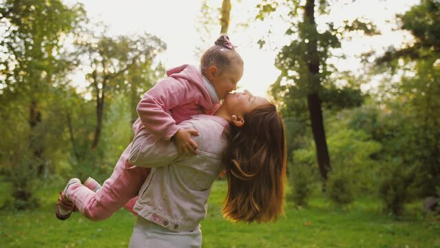 Adorable little daughter hugging mother with, and kissing her. Happy affectionate family, cute child embracing mom, cuddling enjoy, tender sweet moment of love in summer park