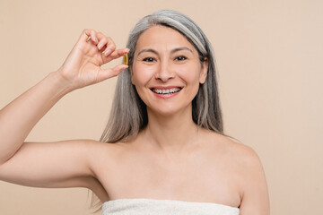 Smiling mature middle-aged caucasian naked shirtless woman holding a pill for beautification,...