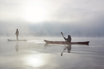 Two women paddling kayak and stand up paddle board (SUP) at autumn misty river at foggy autumn...