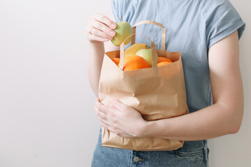shopping, healthy eating and eco friendly concept - close up of woman holding eco bag with fruits on white background