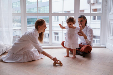 Cute family of father, mother and daughter smiling, playing and joking together. Family playing at window with toy, girl flying