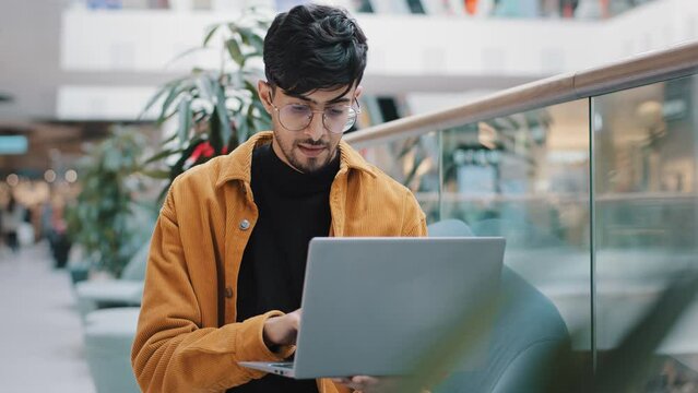 Young indian man looking at laptop screen checking email smiling enjoying free time browsing web page on dating site making order in online store chatting on social media using computer application