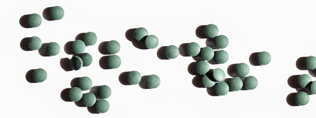 natural additives and superfood. green spirulina algae pills on white background with shadow. healthy lifestyle concept. organic food banner