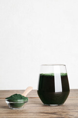 fresh green drink with spirulina in glass, spirulina powder with spoon on wooden background. useful habits, self care and healthy lifestyle.copy space