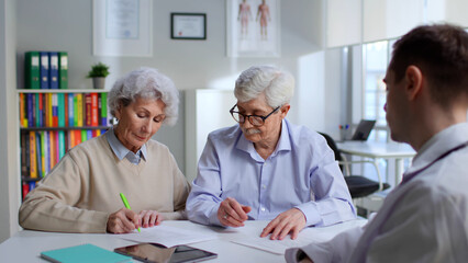 Senior couple sign document in doctor office