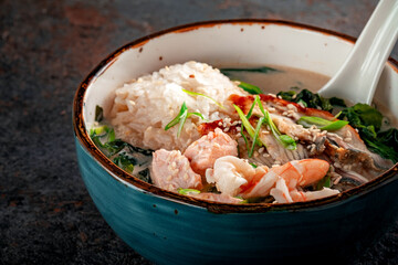 Oriental seafood soup with cream in a blue ceramic bowl. Fish Soup with salmon, eel, shrimp, rice, onion, sesame and seaweed, close up