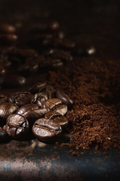 Fragrant freshly roasted coffee beans and ground coffee are scattered on a metal tray. Close-up, selective focus, vertical frame. © Ed