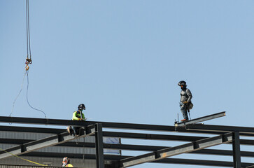 Construction workers with safety gear install steel beams on a commercial building framework, illustrating high-rise structural assembly and occupational safety in commercial development © Eduardo Barraza