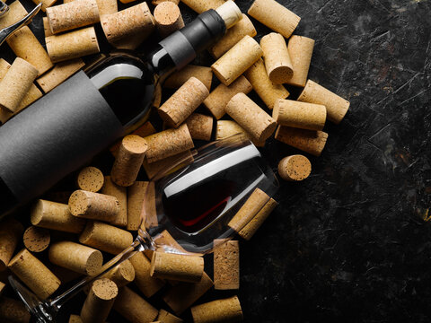 A bottle of red wine and a wine glass with wine lie on wine corks. Isolated on a dark background. There are no people in the photo. There is free space to insert. Restaurant, hotel, bar.