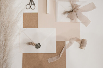 Top view of composition of sheets of paper, scissors, white envelope with grey wax seal, bow of transparent ribbon.