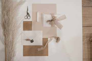 Top view of composition of white, pink sheets of paper, scissors, white envelope with wax seal, bow...