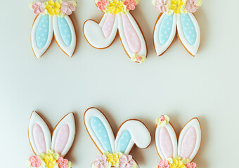 Gingerbread cookies in the shape of cute Easter bunny ears decorated with festive icing and flowers on the white background. Flat lay