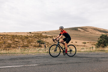 Fototapeta na wymiar Side view of professional cyclist practicing on a countryside road against a hill