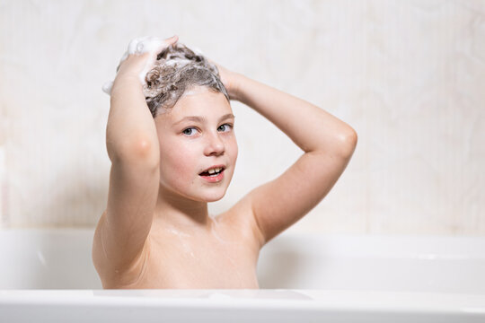 Little, beautiful girl, baby bathes sitting in a white bath with soap suds, shampoo and washes her head with hair. Model photography.
