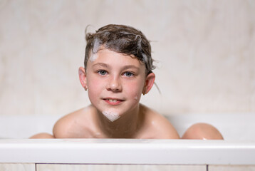 Little, beautiful girl, baby bathes sitting in a white bath with soap suds, shampoo and washes her head with hair. Model photography.