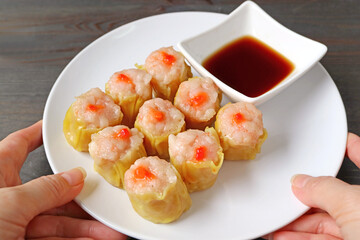 Hand Placing a Plate of Shrimp and Pork Filled Chinese Steamed Dumplings or Shumai on Wooden Table