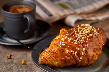 Croissant, coffee and newspaper on dark stone table