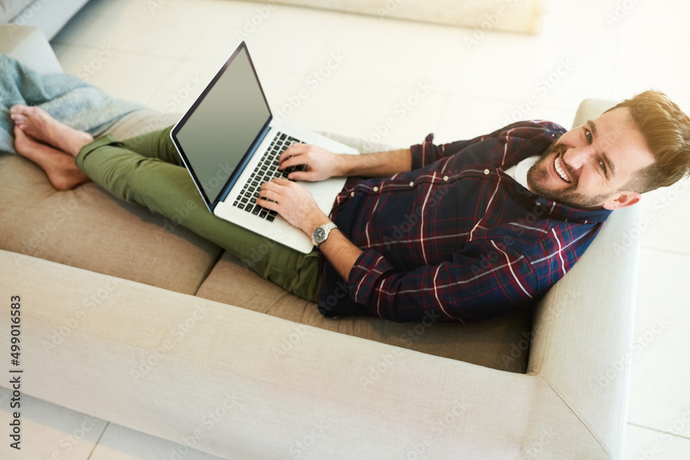 Poster All I need for a lazy day at home. Shot of a relaxed young man using a laptop on the sofa at home.