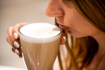 Close-up of beautiful female hands holding a large white cup of cappuccino. A woman is sitting in a cafe.