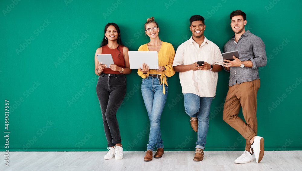 Poster Were always in the loop. Portrait of a group of young designers using digital devices while standing together against a green background.