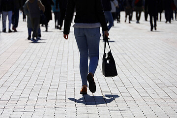 Girl in jeans walking with handbag on a city street on crowd of people background. Concept of...