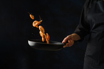 Tiger prawns in a pan in a frozen flight on a black background in the hand of a professional chef. Sea food. Recipes for restaurant and home cooking. Cookbook, food blog. Advertising, invitation. © Anton