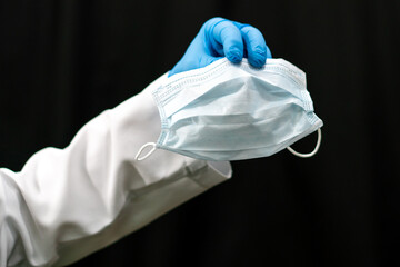 A doctor in a white coat holds a white medical mask in his hand. Gauze bandage as a means of combating coronavirus infection. Treatment and prevention of respiratory infections.