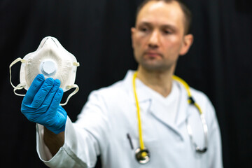 A doctor in a white coat holds a white medical mask in his hand. Gauze bandage as a means of combating coronavirus infection. Treatment and prevention of respiratory infections.