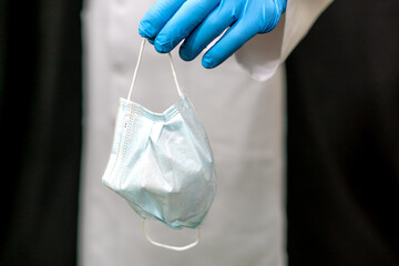 Blue medical glove and mask on a white background. A doctor wearing gloves holds a protective mask against viral infections in his hands
