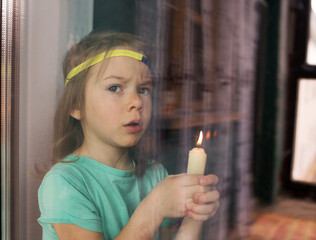 a sad little girl is standing behind the glass with a candle in her hand