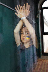 a sad little Ukrainian girl is standing behind the glass with her hands tied up. The children of...