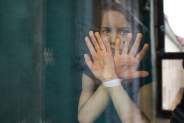 a sad little Ukrainian girl is standing behind the glass with her hands tied up. The children of...