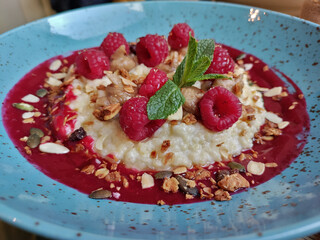 Detail of muesli breakfast with raspberry jam, raspberries, mint, and seeds. The food is served on the beautiful blue decorative plate.