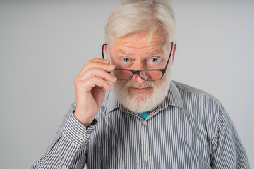portrait  elder senior man holding eyeglasses, with a beard and gray hair looks from under forehead and holds glasses with his hands.