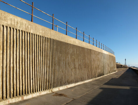 concrete seawall and railings along the pedestrian promenade in north blackpool with the tower and town in the distance in afternoon sunshine